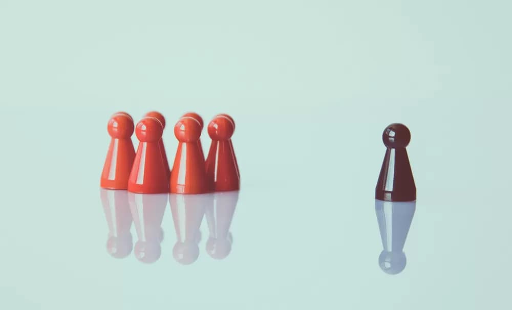 Group of red pawn figures standing apart from a single dark red pawn on a pale surface, illustrating the choice of the right CDMO partner