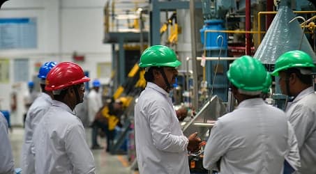 Team members in hard hats and lab coats discussing process steps on a peptide manufacturing plant floor